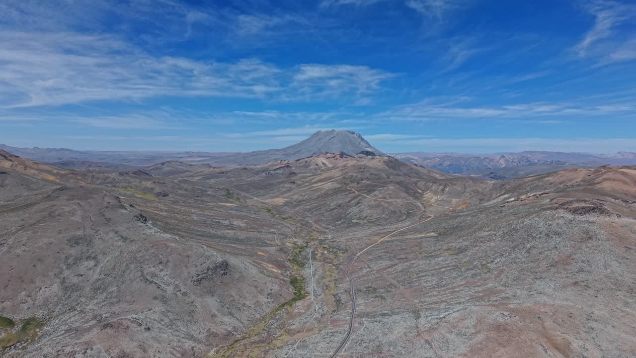 Una valle incredibilmente brulla si estende verso l'imponente vulcano Pucasaya nel Parco Nazionale Laguna Salinas, Perù. Cieli azzurri e radiole nuvole bianche aleggiano su un paesaggio vulcanico segnato.