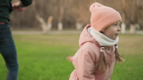 분홍색 재과 베니를 입은 어린 소녀가 즐겁게 회전하고 울창한 초록색 에서 놀고 있으며, 배경에는 부분적으로 보이는 남자가 놀이에 참여하고 있습니다.