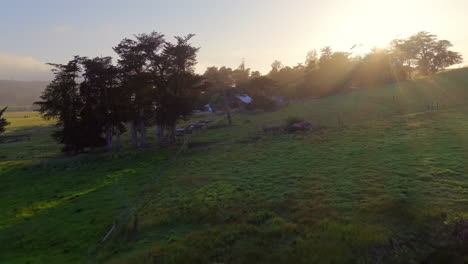 vista aérea baja de los rayos del sol vespertino sobre el campo rural con una pequeña casa en las colinas
