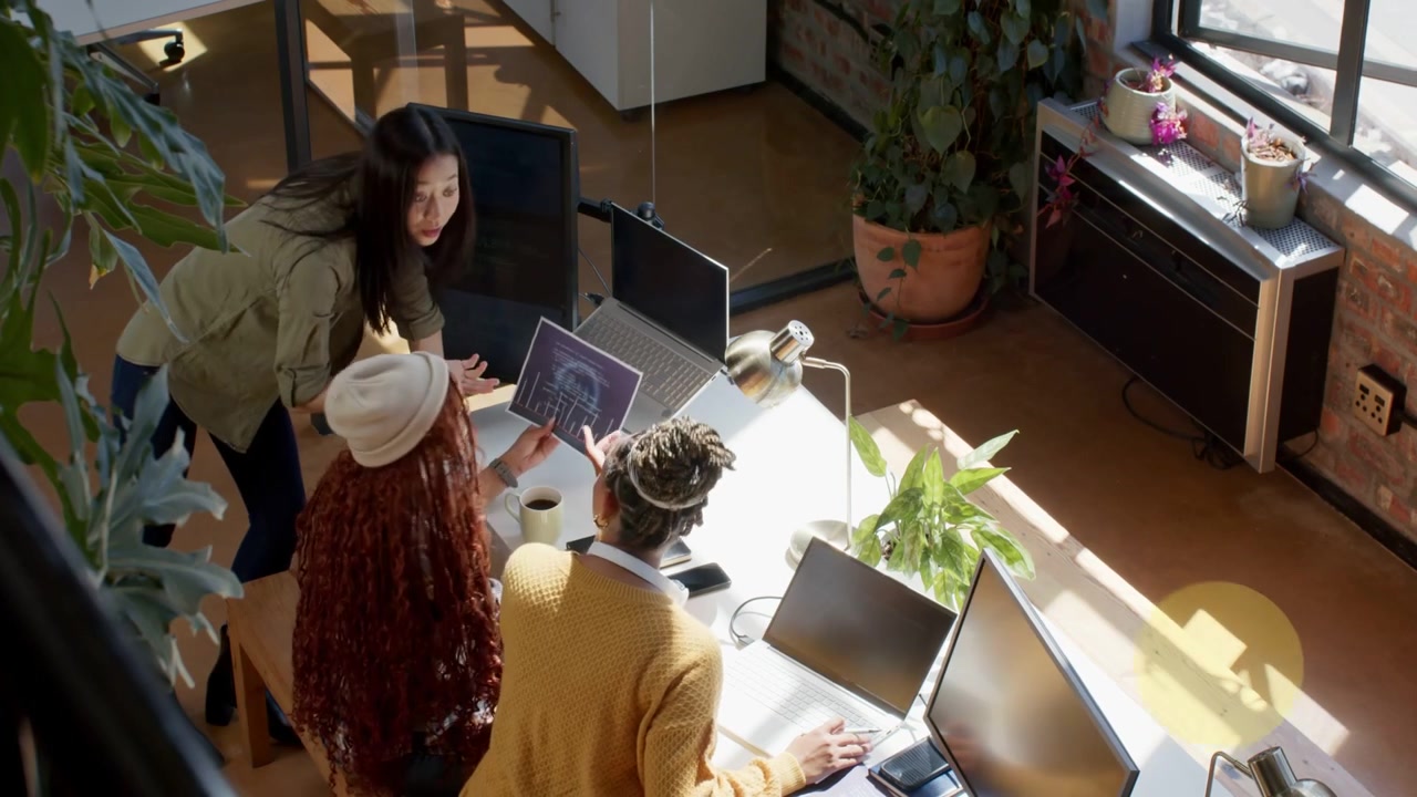 Designers around desk reviewing chart, woman pointing tablet causing bokeh growing, moving, fading