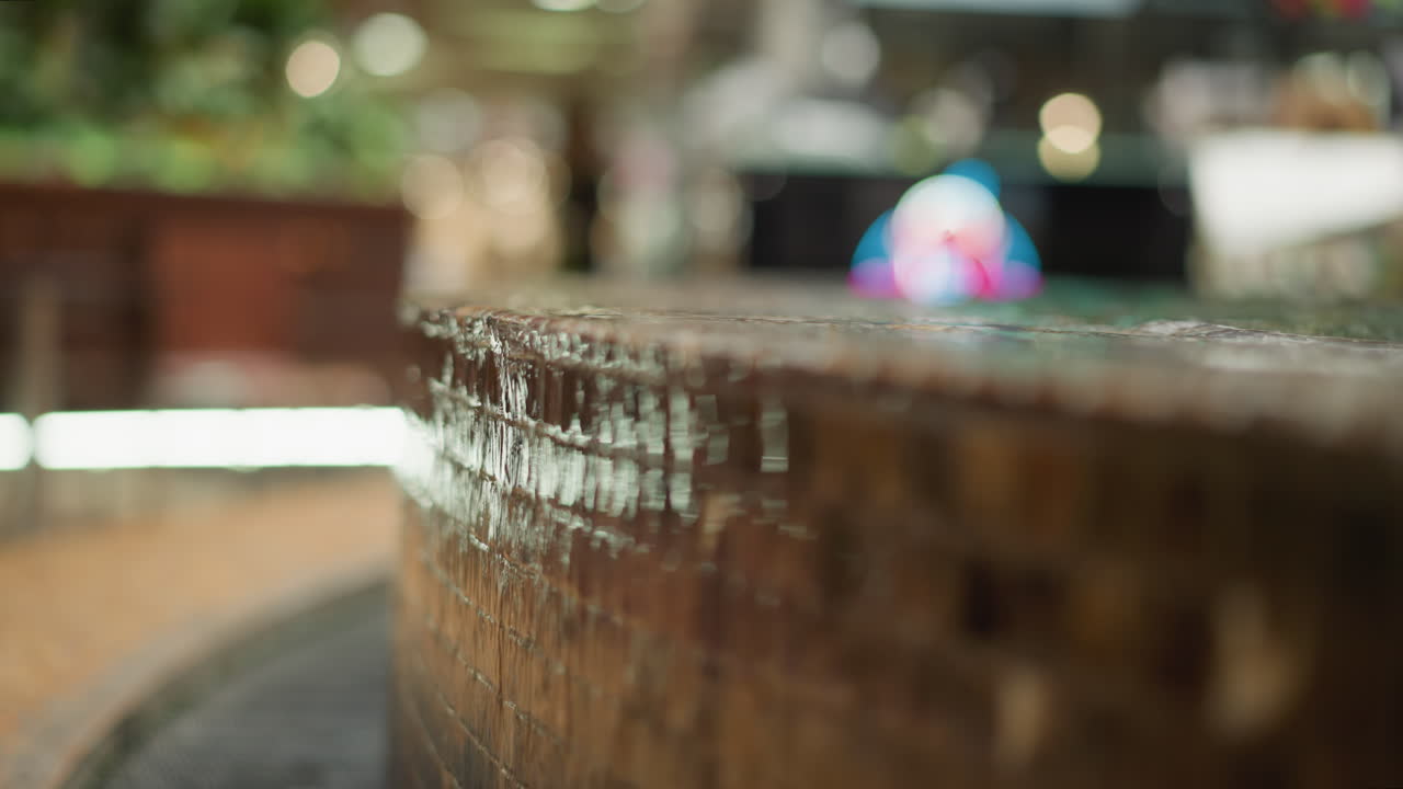 primer plano de agua en cascada por un borde de fuente texturizado y azulejos con fondo borroso con luz ambiental y un objeto colorido y poco claro
