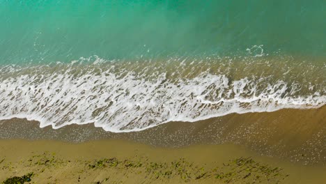 Sea-shore-with-yellow-sand-splashed-by-white-sea-waves-foaming-from-turquoise-lagoon-on-Mediterranean-seaside