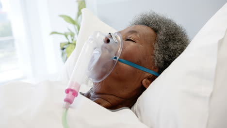 african american senior female patient with oxygen mask lying in bed in hospital room, slow motion