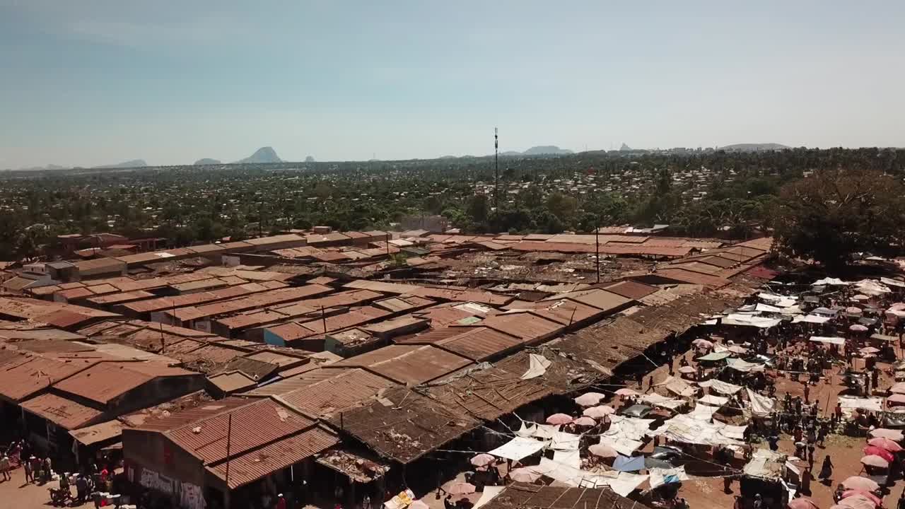 Aerial cityscape of Nampula, Mozambique showing a dense open-air market with rows of tin-roofed stalls and crowds gathered along the market edge