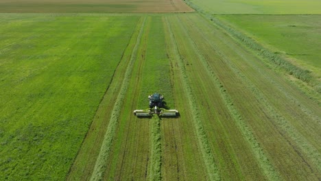 Luftaufnahme-Eines-Traktors,-Der-Ein-Frisches-Grünes-Grasfeld-Mäht,-Eines-Landwirts-In-Einem-Modernen-Traktor,-Der-Futter-Für-Nutztiere-Zubereitet,-Sonniger-Sommertag,-Breiter-Drohnenschuss,-Der-Sich-Vorwärts-Bewegt,-Nach-Unten-Geneigt