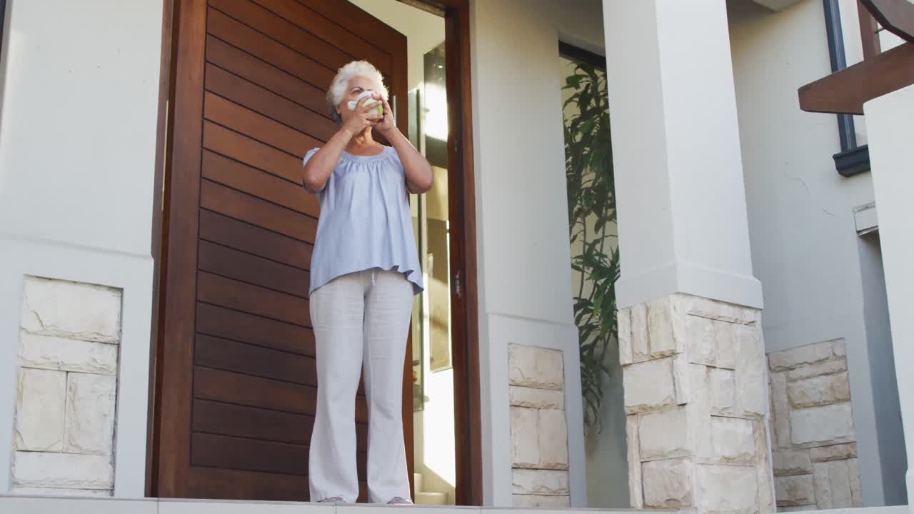 African american senior woman drinking coffee while standing at the front door at home
