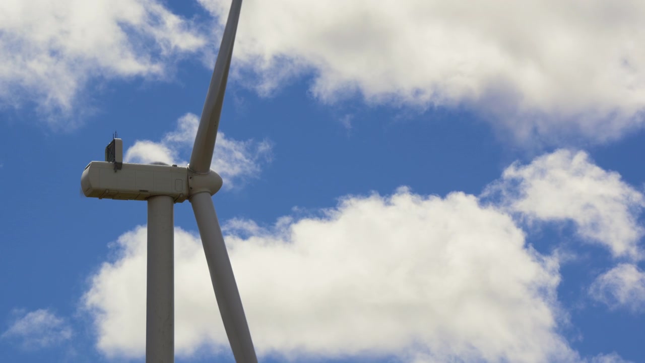 Turbina eolica in rotazione contro un cielo blu con nuvole