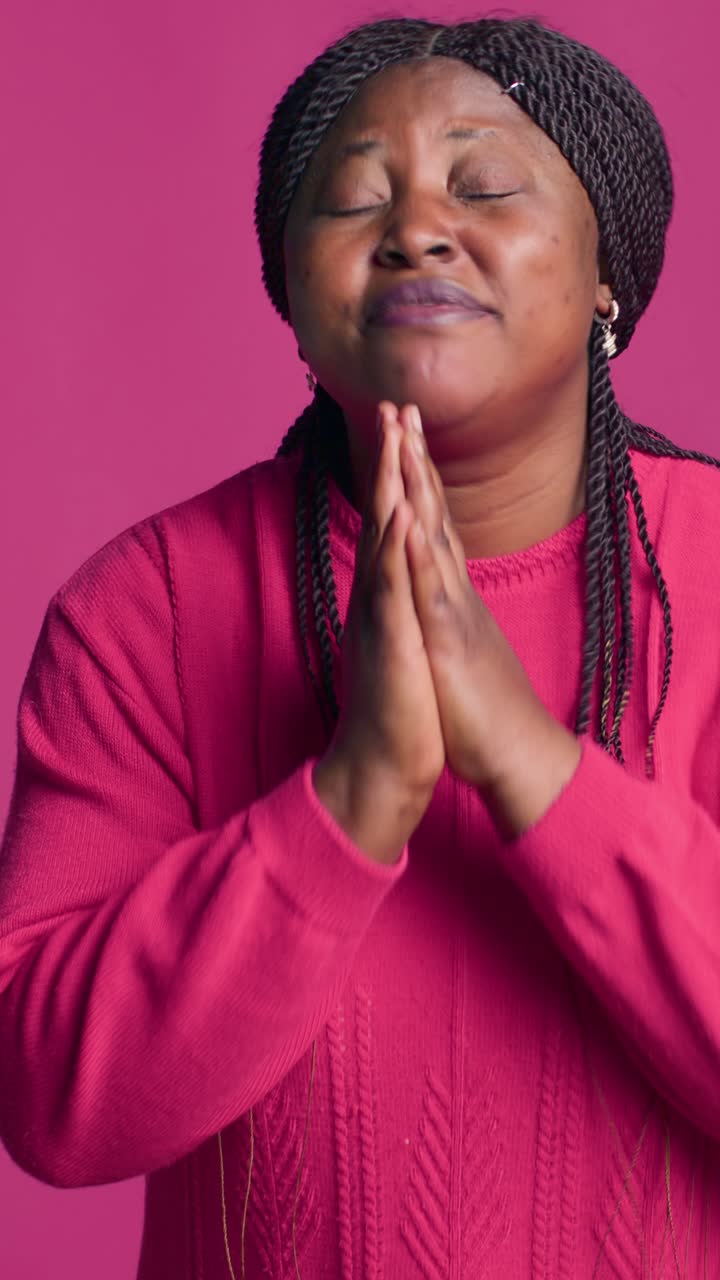 Woman with braids praying on pink background