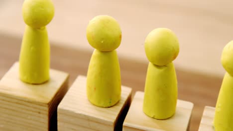 yellow figurines on wooden blocks in a row and red figurine fallen on ground