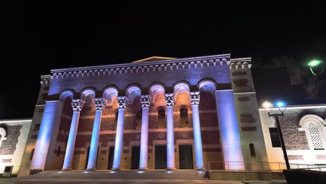 Moving-cinematic-shot-of-a-historic-building-illuminated-by-blue-and-purple-lights-at-night