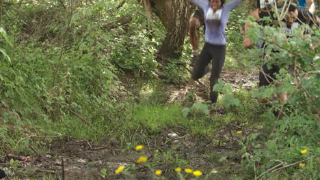 Assault-course-competitors-running-through-forest,-low-angle