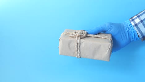 hand in blue gloves holding a wrapped gift box