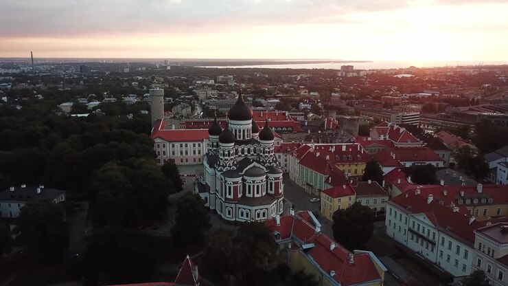 Filmato mozzafiato con drone del Centro Storico medievale di Tallinn al tramonto. L'inquadratura mostra la Collina di Toompea, la Cattedrale di Santa Maria e gli edifici dai tetti rossi sotto un cielo drammatico di nuvole rosa e arancioni.