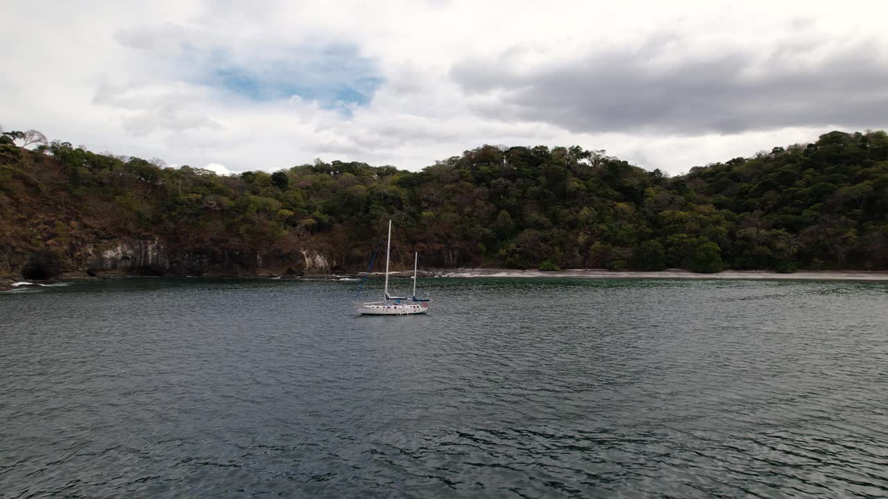 Drone flying towards white sailboat sailing along tropical coast of Costa Rica's beaches