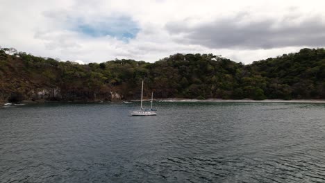 Drone-flying-towards-white-sailboat-sailing-along-tropical-coast-of-Costa-Rica's-beaches