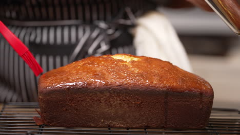 brushing a sweet glaze on a lemon pound cake fresh out of the oven