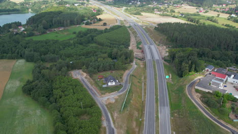 Toma-Aérea-Ascendente-De-La-Carretera-Vacía-En-La-Zona-Rural-De-Polonia-Con-árboles-Forestales-Y-Lago