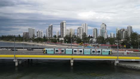 Moving-Aerial-view-of-a-busy-mains-road-bridge-spanning-across-a-popular-waterway-with-a-city-skyline-in-the-background