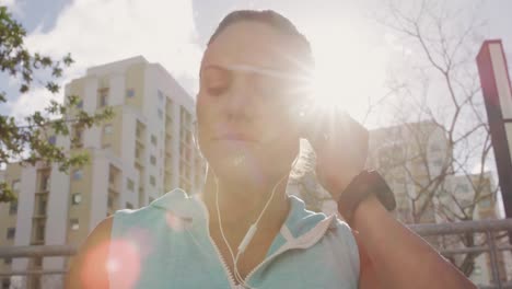 mujer caucásica deportiva poniendo sus auriculares al aire libre