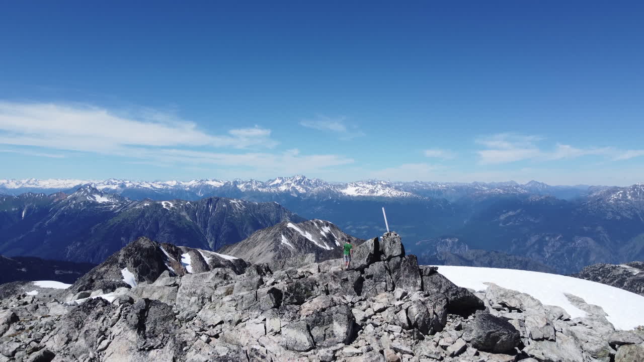 el escalador alcanza el marcador de la cima de la montaña con una vista increíble sobre el paisaje rocoso cerca del pan de azúcar de los prados de pemberton - imágenes aéreas de drones