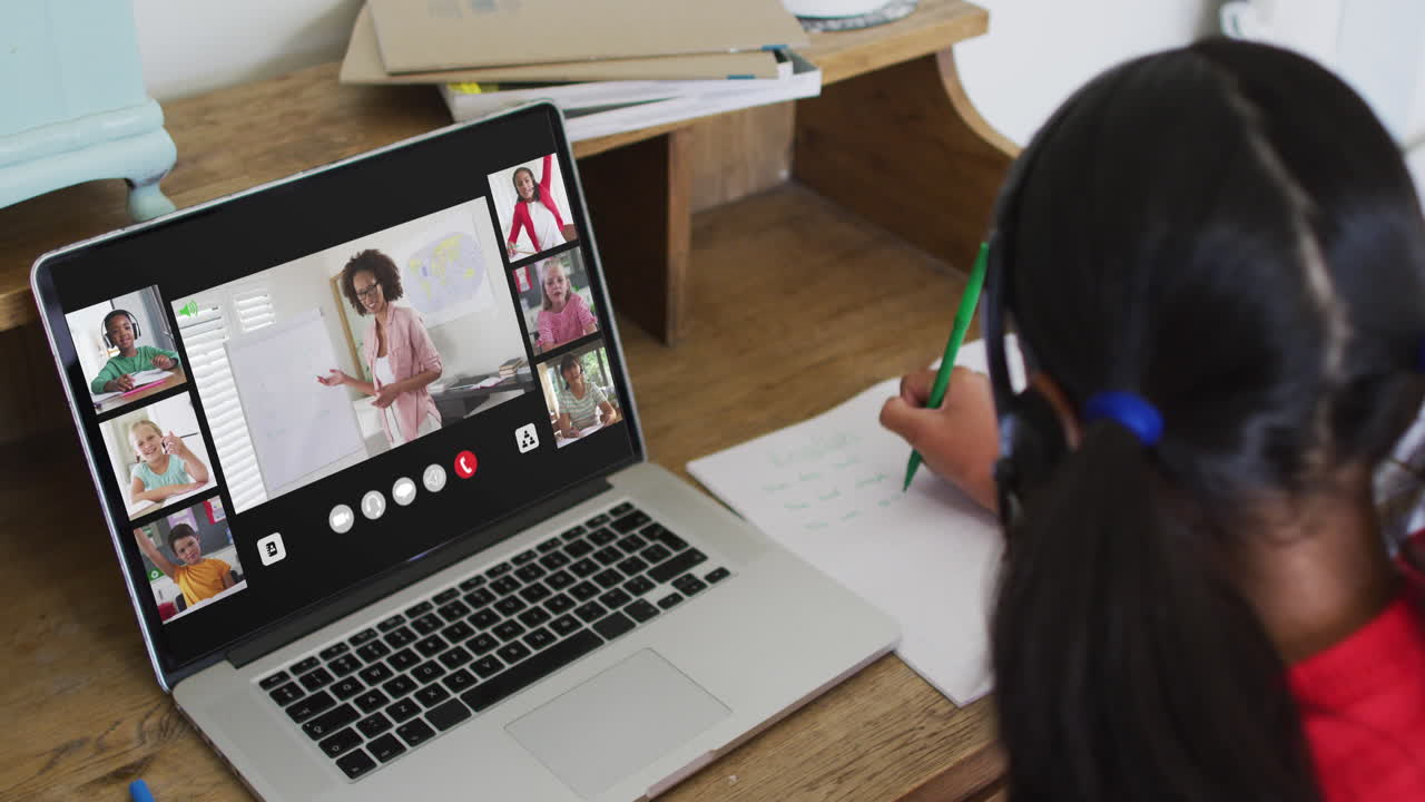 Schoolgirl using laptop for online lesson at home, with diverse teacher and class on screen
