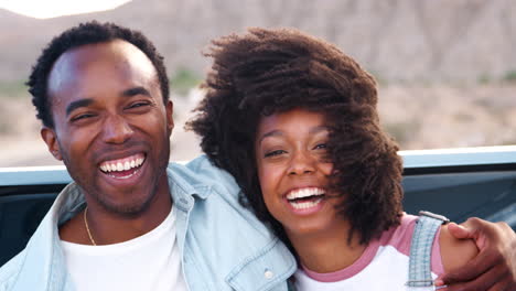 Laughing-young-couple-on-road-trip-sitting-on-car,-close-up