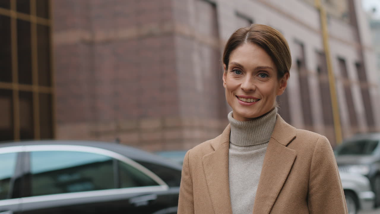 Close-up view of caucasian businesswoman wearing elegant clothes looking and smiling to the camera in the street in autumn