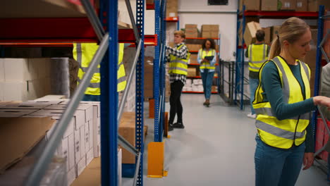 Team-Leader-With-Digital-Tablet-In-Busy-Warehouse-Training-Female-Intern-Standing-By-Shelves