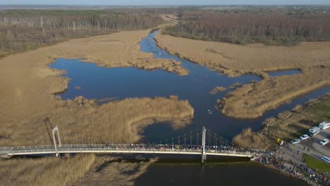 gorgeous aerial drone video flying over kayaks and paddleboards rowing and paddling forward during a marathon on a dark colored blue river that is surrounded by brown reeds and grass, sunny day.
