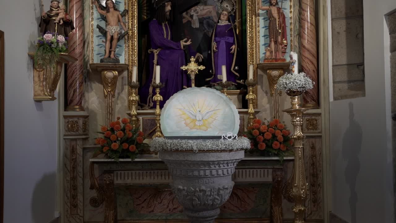 Catholic church altar showing Jesus Christ statues saints candles flowers and font