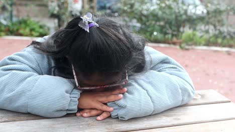 a young girl sitting on a park bench, looking sad.