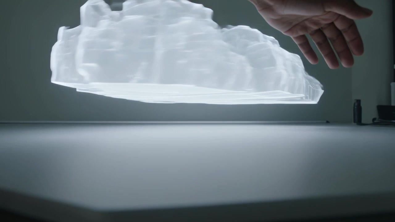 Reaching top-left, bare arm and hand sliding beneath 3D model at light table, tracing contours