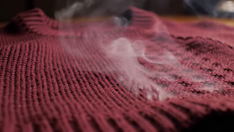 close-up of a maroon sweater with rising steam, capturing the texture and details of the fabric in a cozy atmosphere
