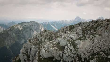 Drone-shot-of-mountain-Rombon,-some-sun-ray-penetrating-the-clouds,-group-of-hikers-climbing-up-the-rocks-to-reach-the-top