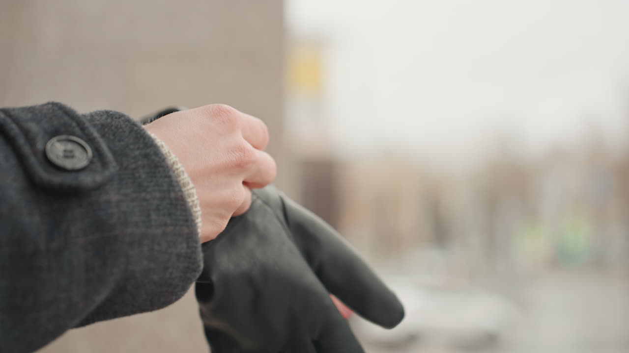Creator photographer putting on black gloves outdoors, closeup of hands sliding into leather gloves, gray wool coat, blurred city background, deliberate slow motion, tactile palm texture and cinematic