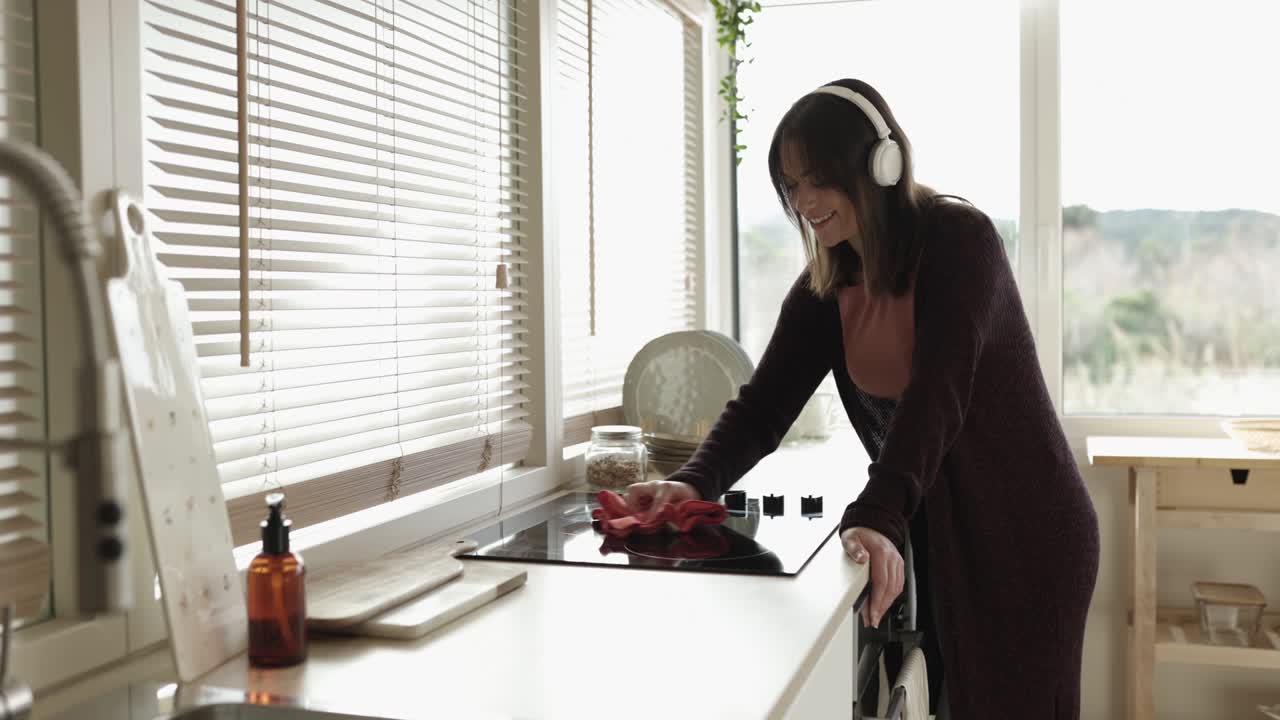 Happy young housewife woman cleaning the kitchen while listening to music