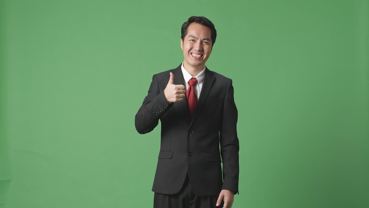아시아 사업가 한 명 이 그린 스크린 스튜디오 에 서 있는 동안 엄지손가락 을 올려 놓고 미소 를 지고 있다
