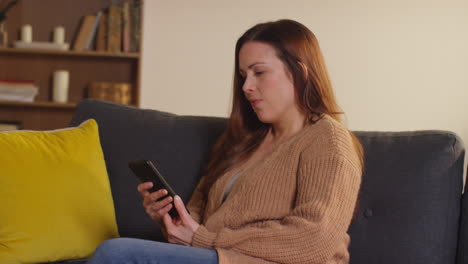 woman sitting on sofa at home at streaming or watching movie or show or scrolling internet on mobile phone 3