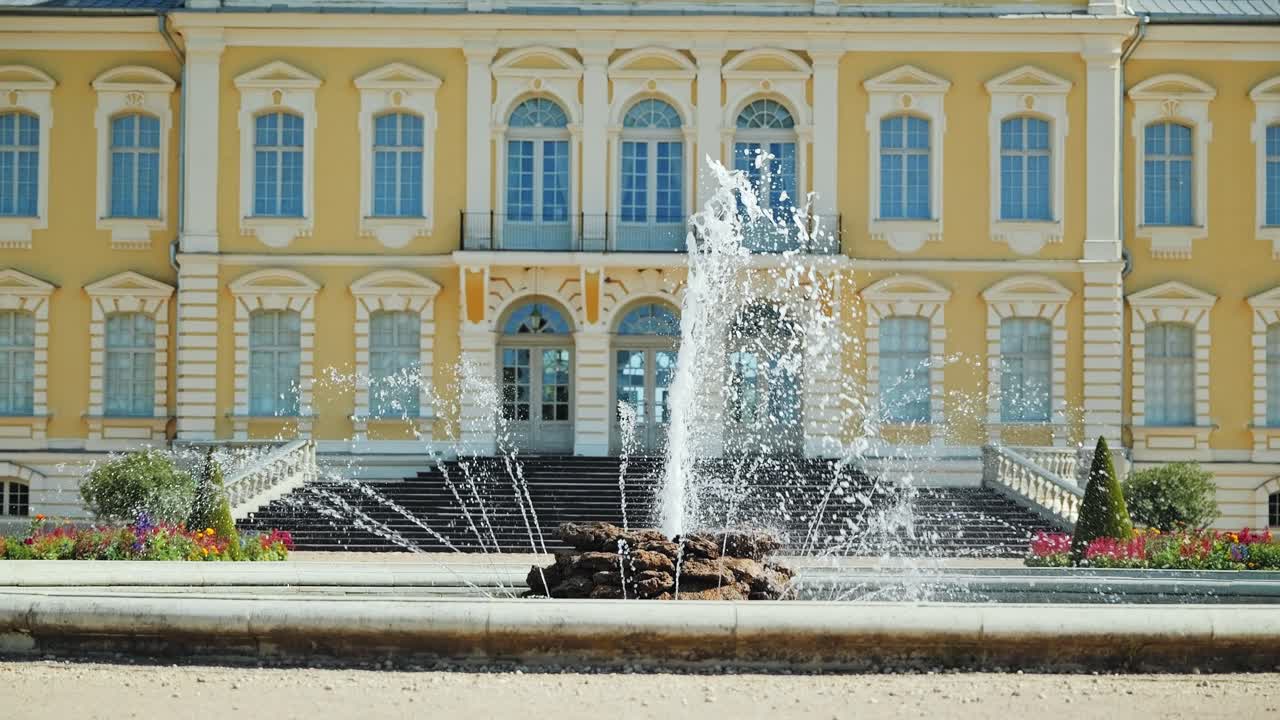 Elegante fuente rociando agua en cámara lenta, fachada barroca del Palacio de Rundale