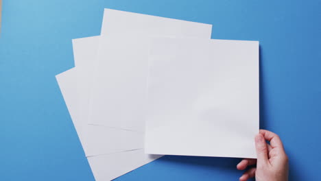 mano sosteniendo un pedazo de papel sobre pedazos de papel con espacio de copia en fondo azul en cámara lenta