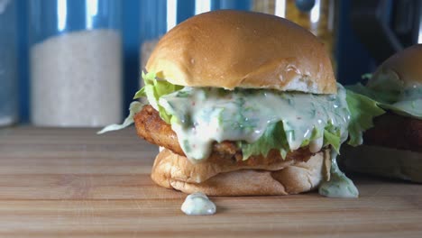 Tiro-De-Seguimiento-En-Cámara-Lenta-De-Crujientes-Deslizadores-De-Pastel-De-Pescado-Casero-En-Una-Tabla-De-Cortar-De-Madera-En-La-Cocina