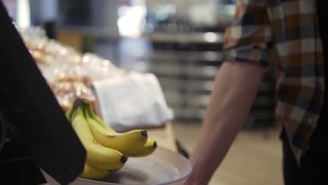 theme health and natural food. close-up of the hand of a man putting on bananas on scale. caucasian man weighing a bunch of bananas. a vegetarian guy buys a yellow fruit