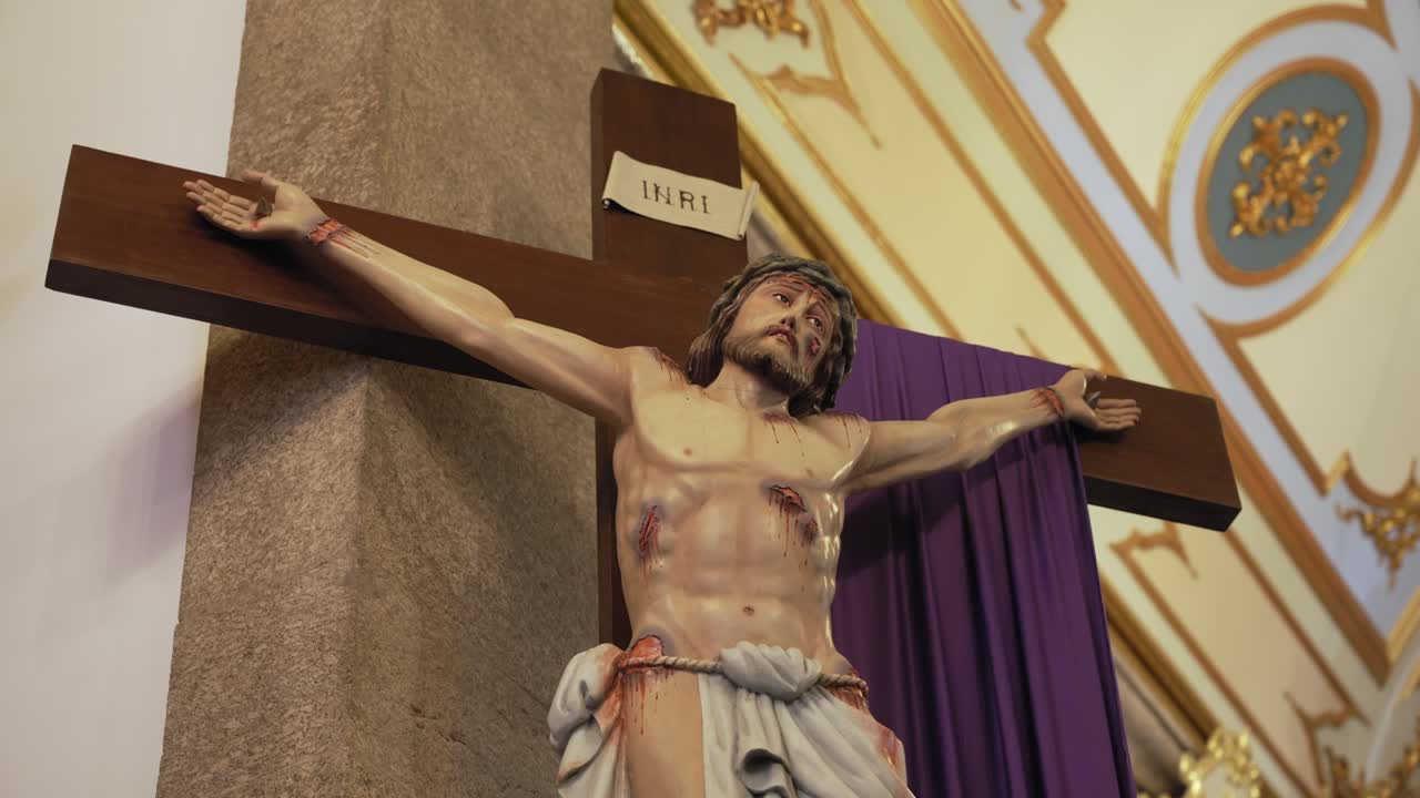 Realistic statue of Jesus crucified on a wooden cross inside a richly decorated church