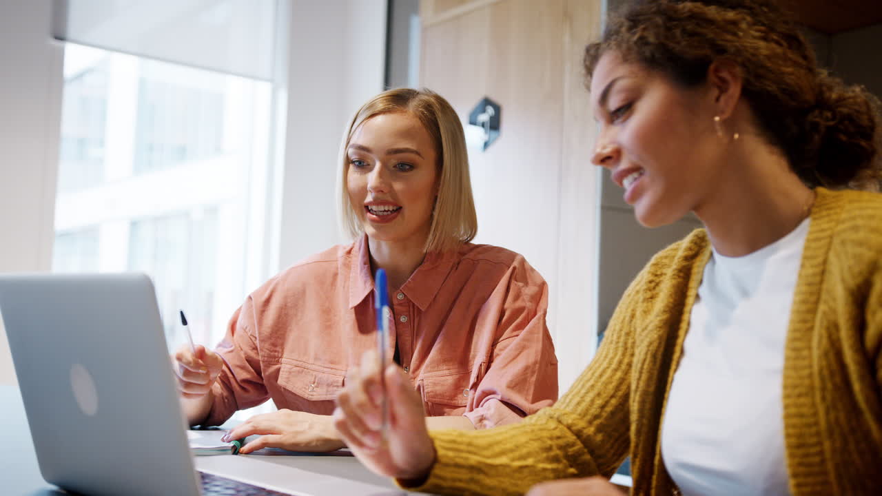 Due giovani creative che lavorano insieme, in discussione davanti a un computer portatile, ripresa dal basso, primo piano