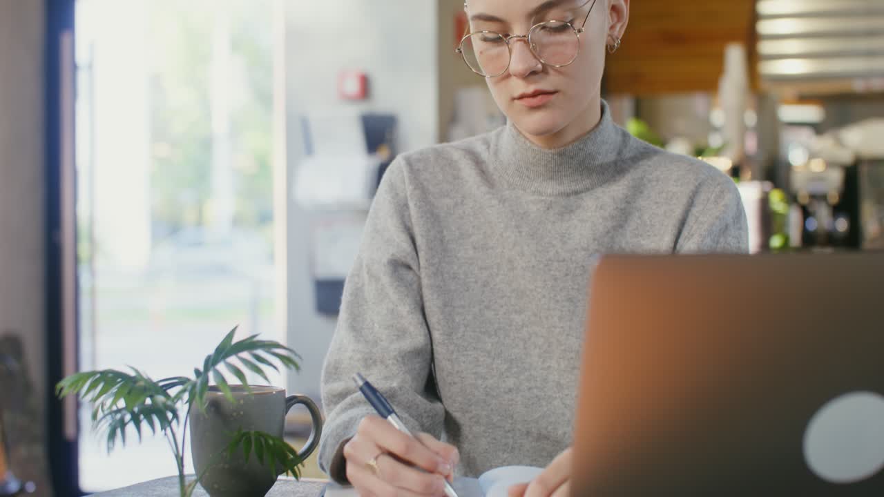 Kvinde arbejder på en café med bærbar computer og notesbog