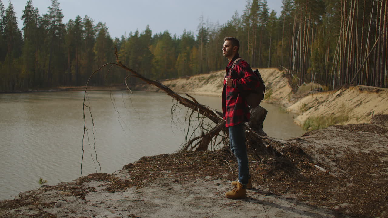 Hiker with a backpack at sunset on the top of a mountain enjoying the sunset with a raised hand in a winner's pose against the background of the river. Travel and vacation concept. High quality 4k footage