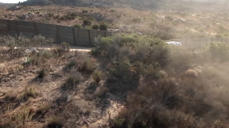 A vehicle travels up a road bordered by a tall fence