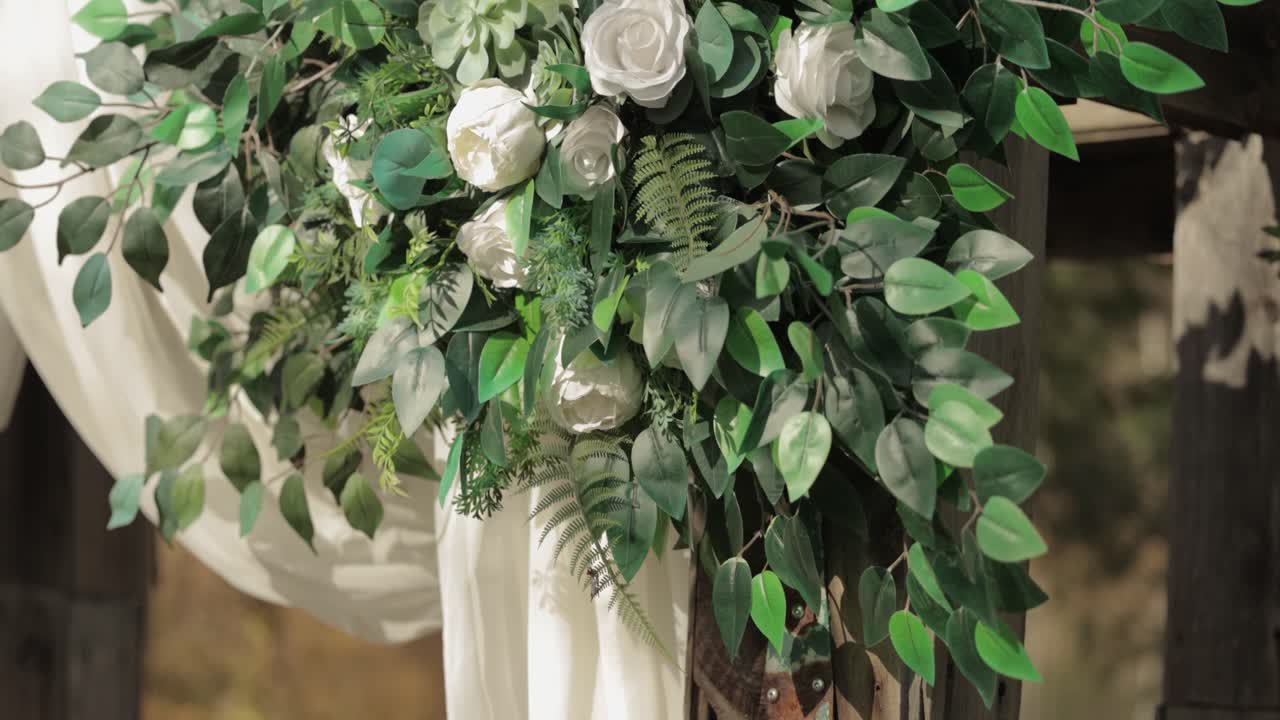Beautiful white rose floral arrangement mounted on a rustic wedding arch at a wedding ceremony at Bean Town Ranch