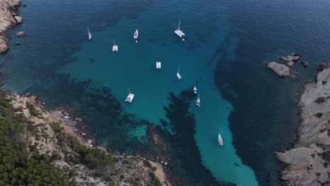 Orbit-shot-flying-over-sailboats-docked-along-seaside-in-Cala-d'egos,-Spain