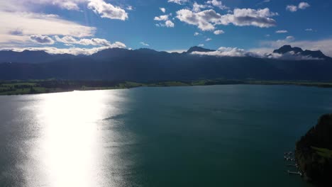 amazing aerial view flying backwards revealing alps with huge mountain range at forggensee in bavaria, germany in 4k